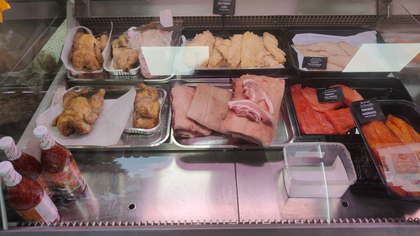 Fish counter with battered cod, fresh whiting, fresh salmon and smoked haddock beside roast chickens and pork belly