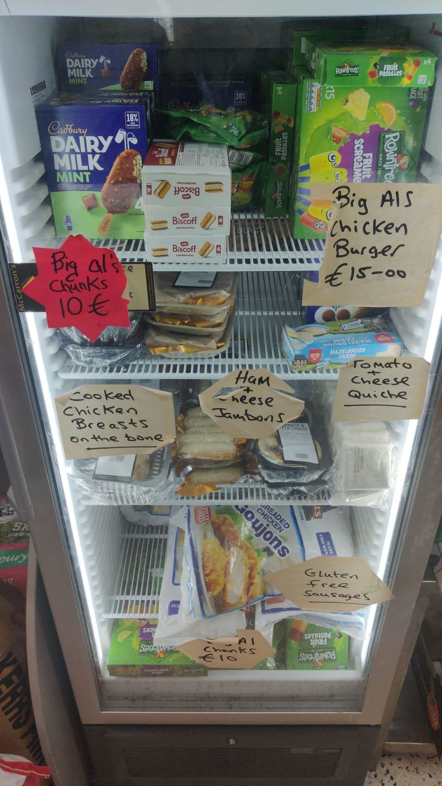 Fridge with handwritten signs for cooked chicken breasts on the bone, ham and cheese jambons, tomato and cheese quiche and gluten-free sausages